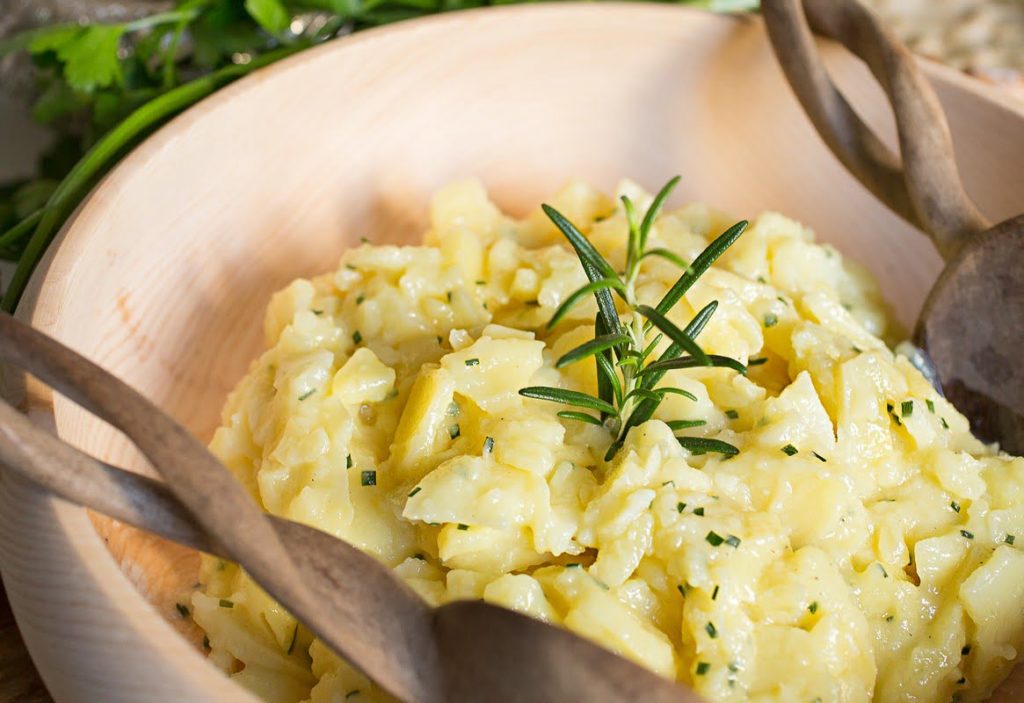 3 Un piatto rustico di patate schiacciate e cremose con rosmarino fresco, servito in una ciotola di legno con cucchiai in legno